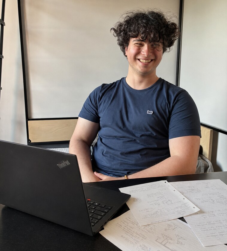 Ilgaz Mehmetoğlu seated behind a ThinkPad and handwritten study notes
